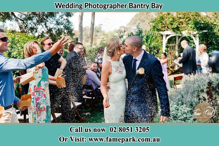 Photo of the Bride and the Groom kissing while showering rice by the visitors Bantry Bay NSW 2087