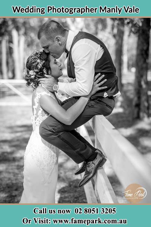 Photo of the Groom sitting on the fence kissing the Bride at the forehead Manly Vale NSW 2093