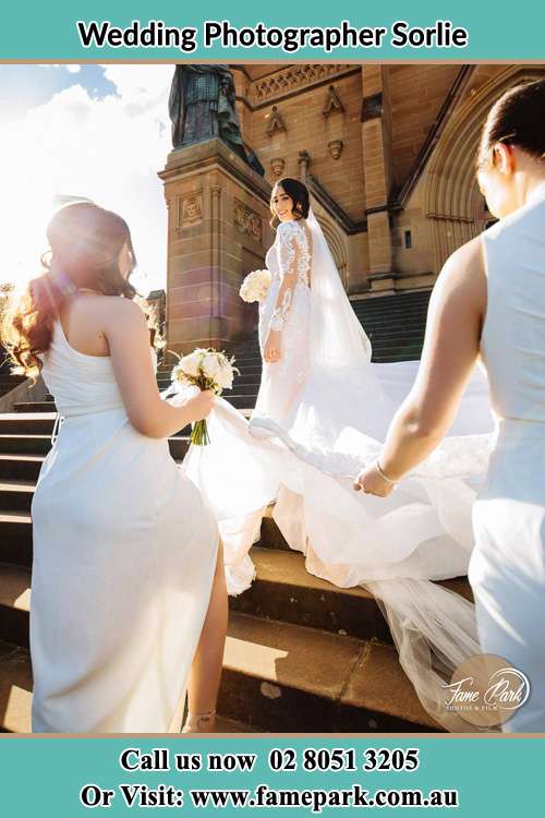 Photo of the Bride smiling at the bridesmaid holding the tale of her wedding gown at the front of the church Sorlie NSW 2086